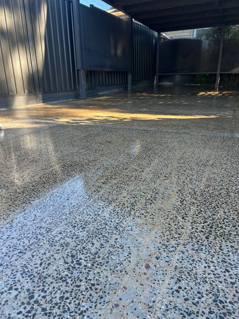 Mirror-polished concrete carport floor reflecting fence and trees