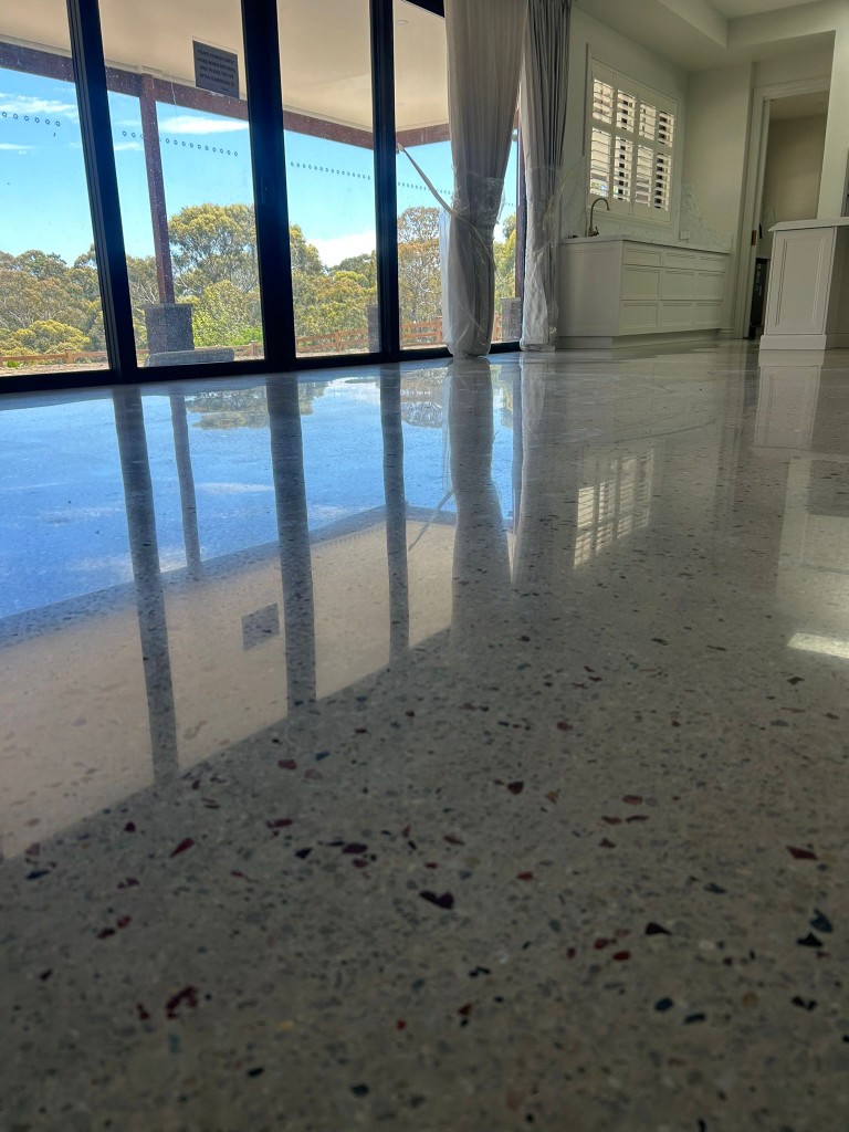 Polished concrete floor with exposed aggregate in open-plan living with kitchen joinery reflections