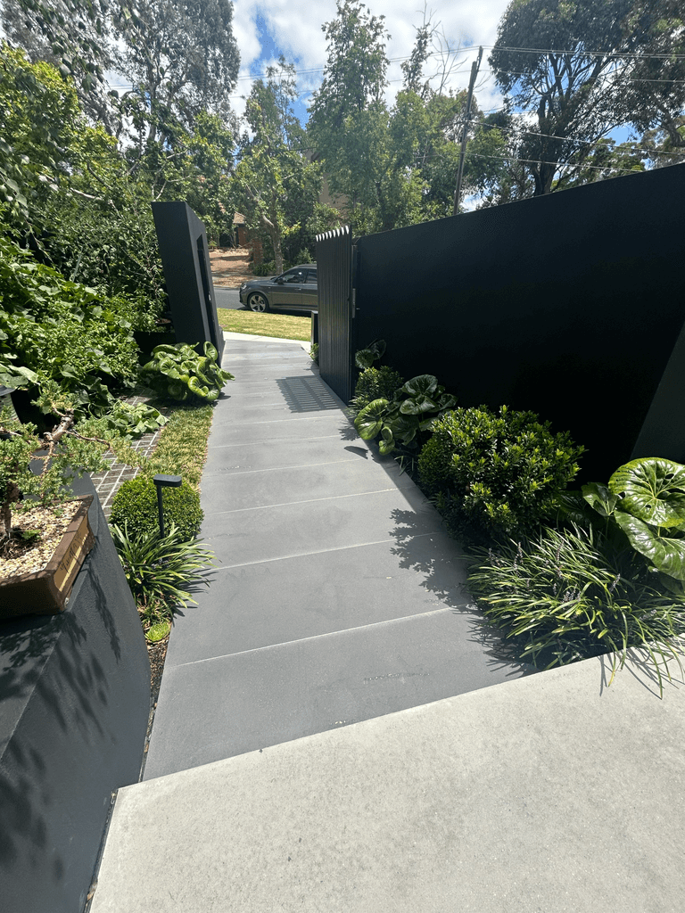 Honed concrete entry path between dark architectural gates at Melbourne residential property