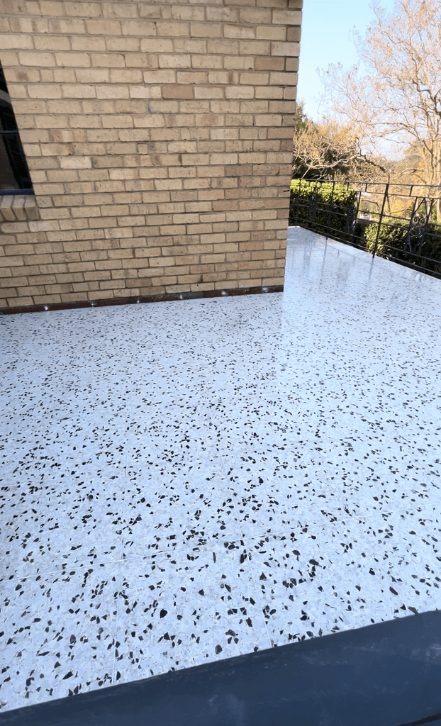 Poured-in-place terrazzo balcony with white base and dense black aggregate, brick wall and garden railing, freshly polished by Claraseal Melbourne