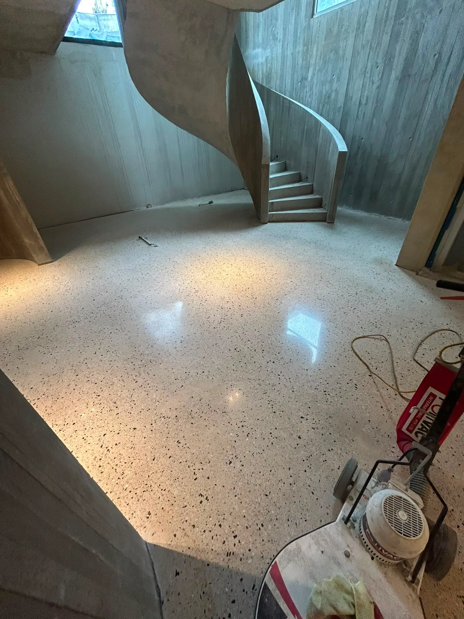 Floor polishing machine in progress in new build with dramatic curved concrete staircase and cream speckle floor, Claraseal Melbourne