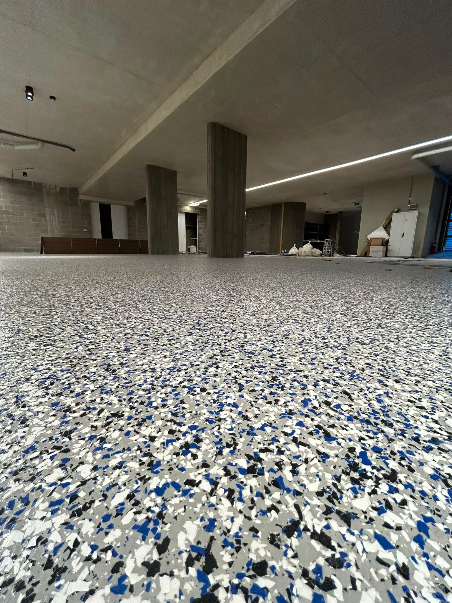 Full-broadcast epoxy flake floor in blue, black, and white in large commercial fit-out