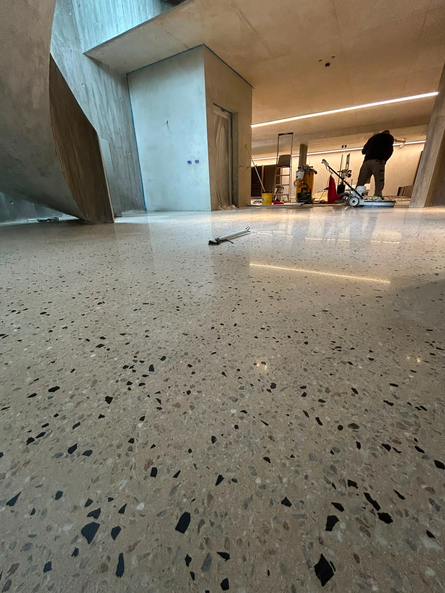 Tradesman operating polishing machine on cream floor with dark aggregate in large commercial space under construction