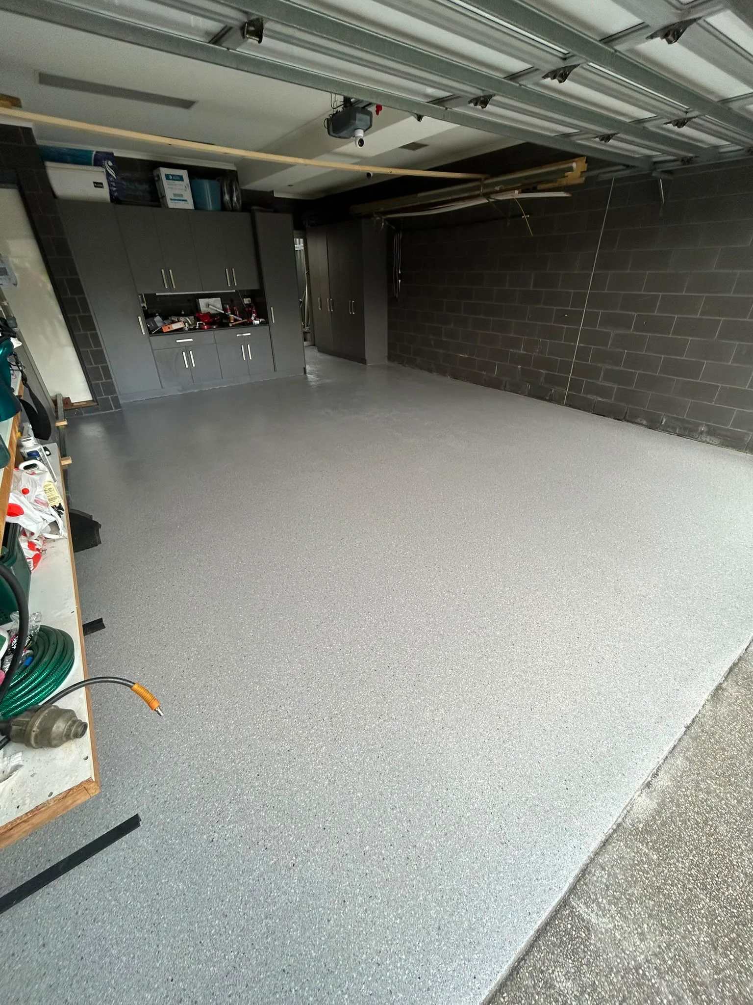 Light grey epoxy flake floor in residential garage with dark grey block-wall and custom cabinetry