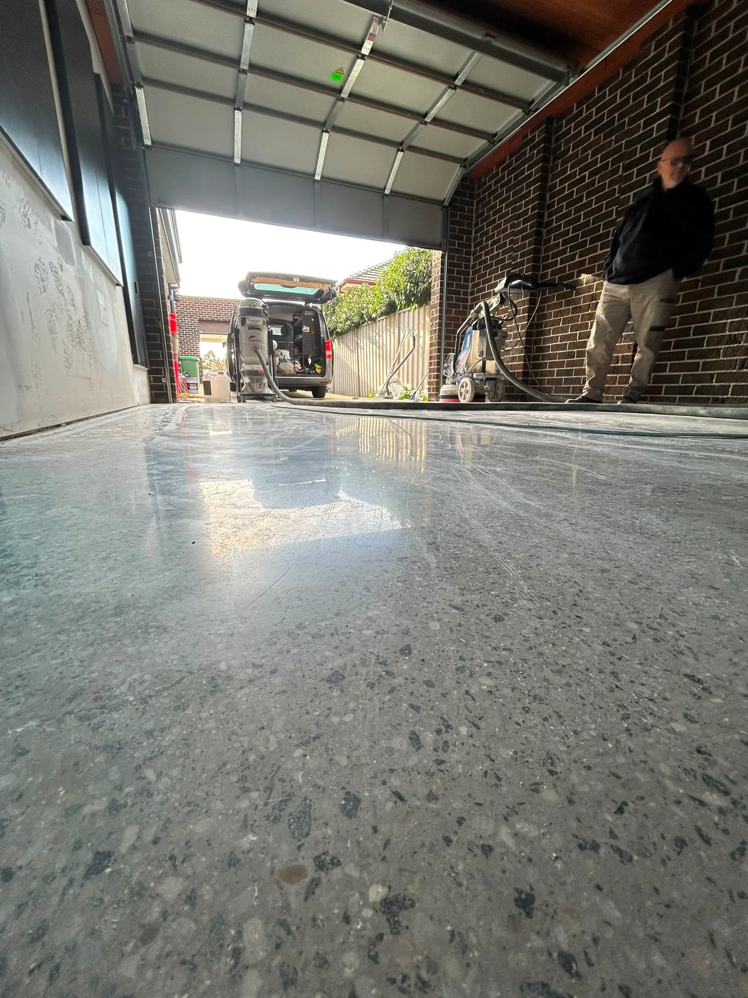 Claraseal work van and tradesman at residential carport, dark grey exposed-aggregate floor during polishing