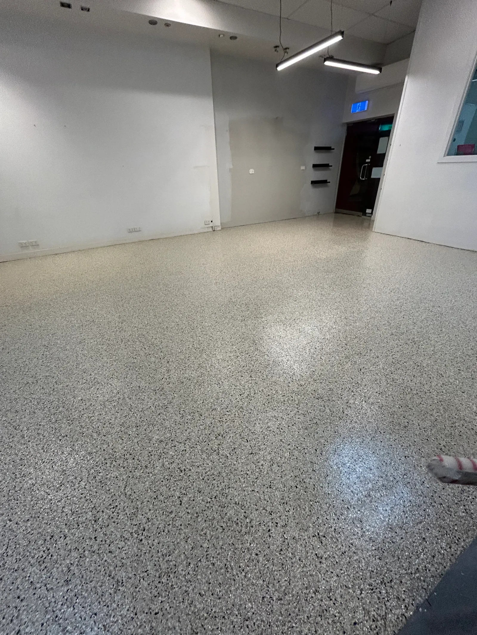 Grey epoxy flake floor with black and white flecks running through an empty Melbourne commercial fit-out to the shopfront door