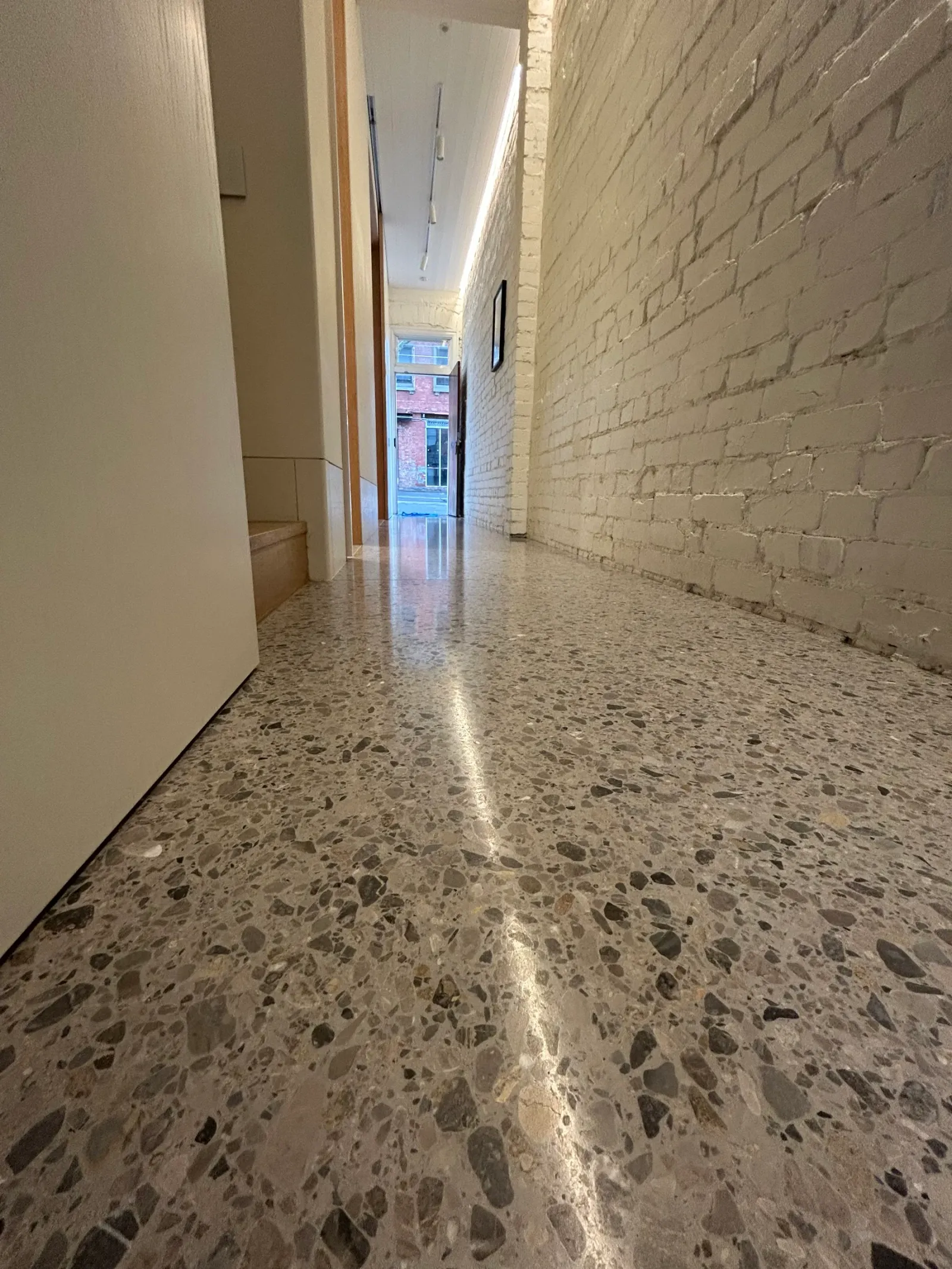 Polished terrazzo hallway with large grey and charcoal aggregate running the length of a white painted brick corridor, Claraseal Melbourne