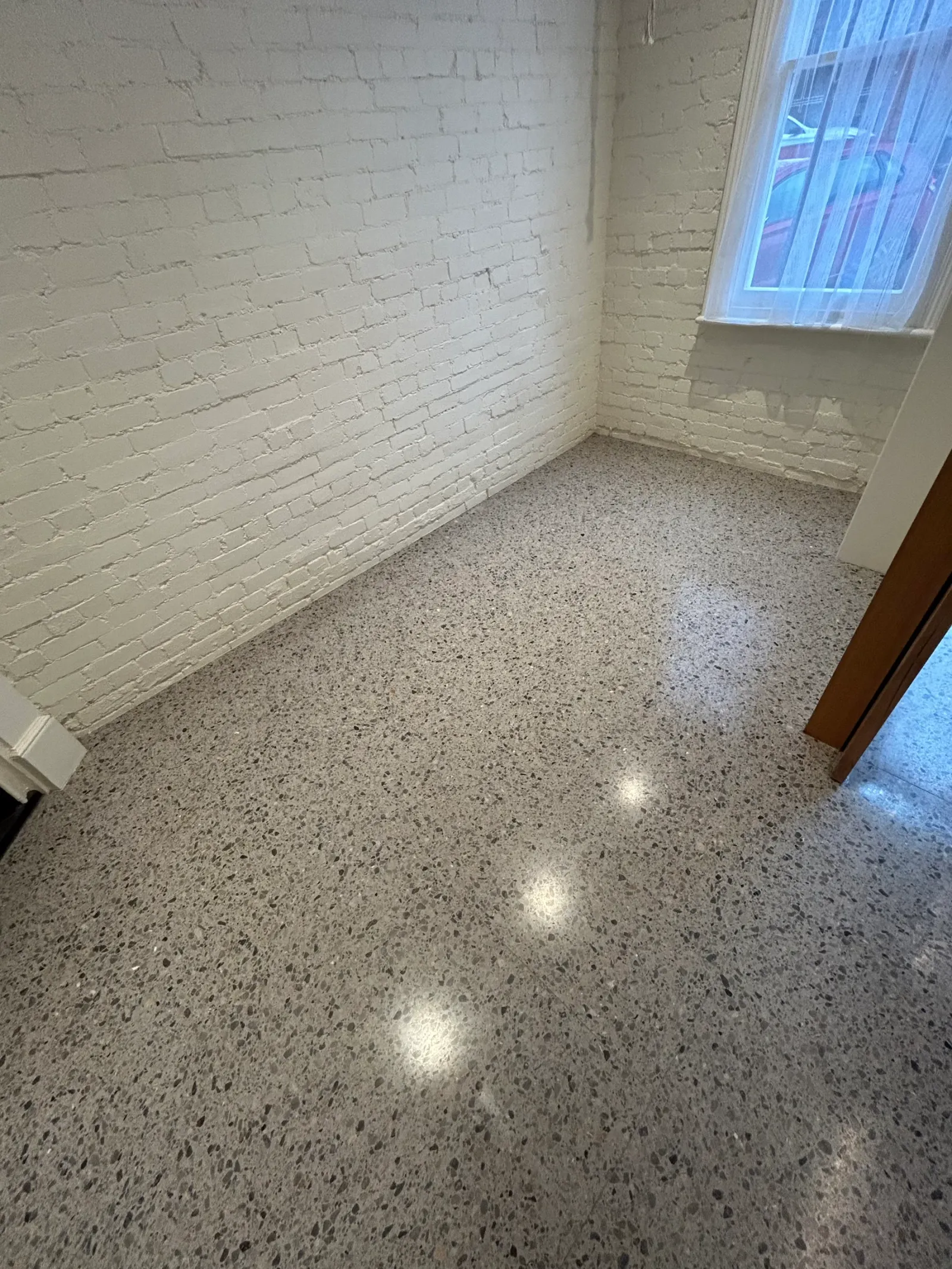 Fine-aggregate terrazzo floor in a white painted brick room, downlights reflecting off the sealed surface