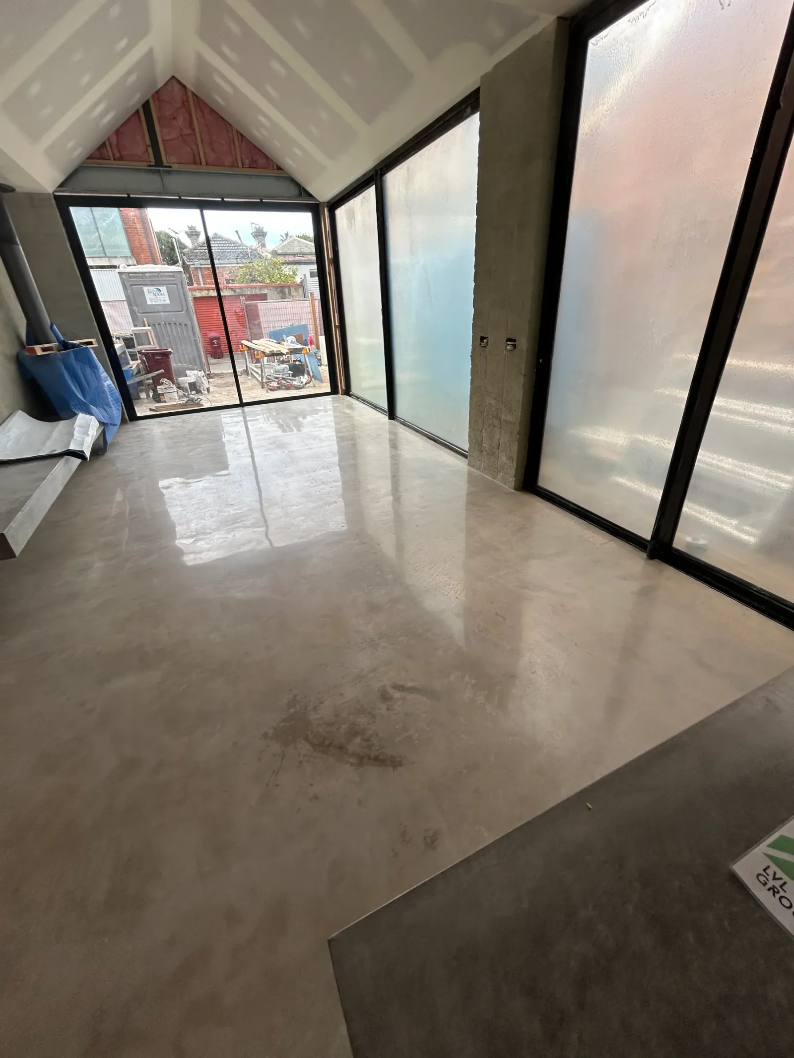 Polished concrete floor with no aggregate exposure, cream mottled finish reflecting a gable ceiling and black-framed glazing in a Melbourne extension