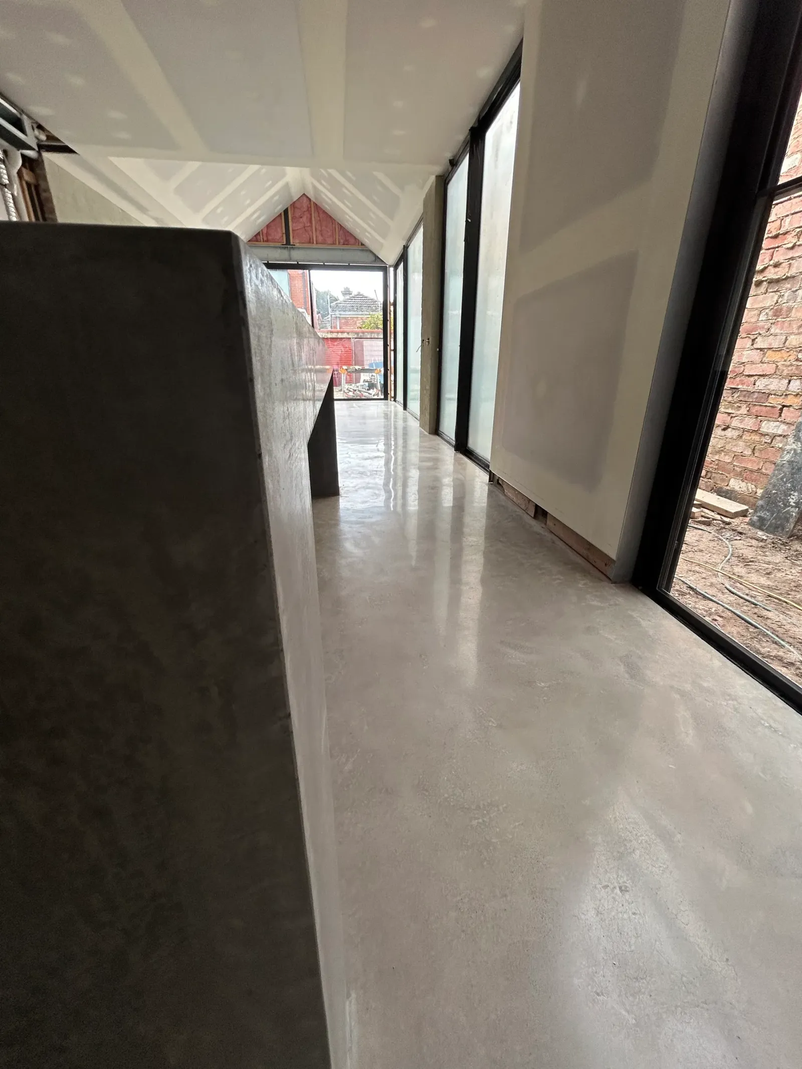 No-exposure polished concrete floor and matching concrete island running through to black-framed glazing and a brick wall beyond