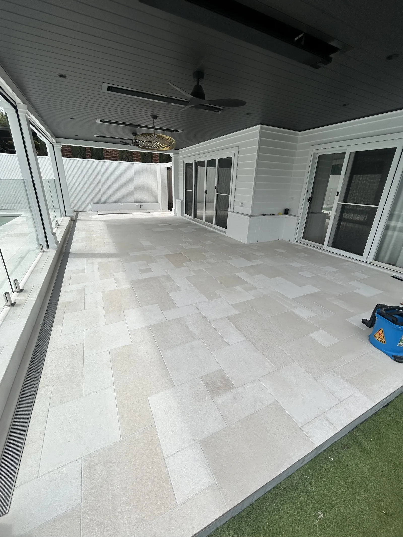 Pale stone pavers in a random pattern under a covered alfresco beside a pool, white weatherboard house