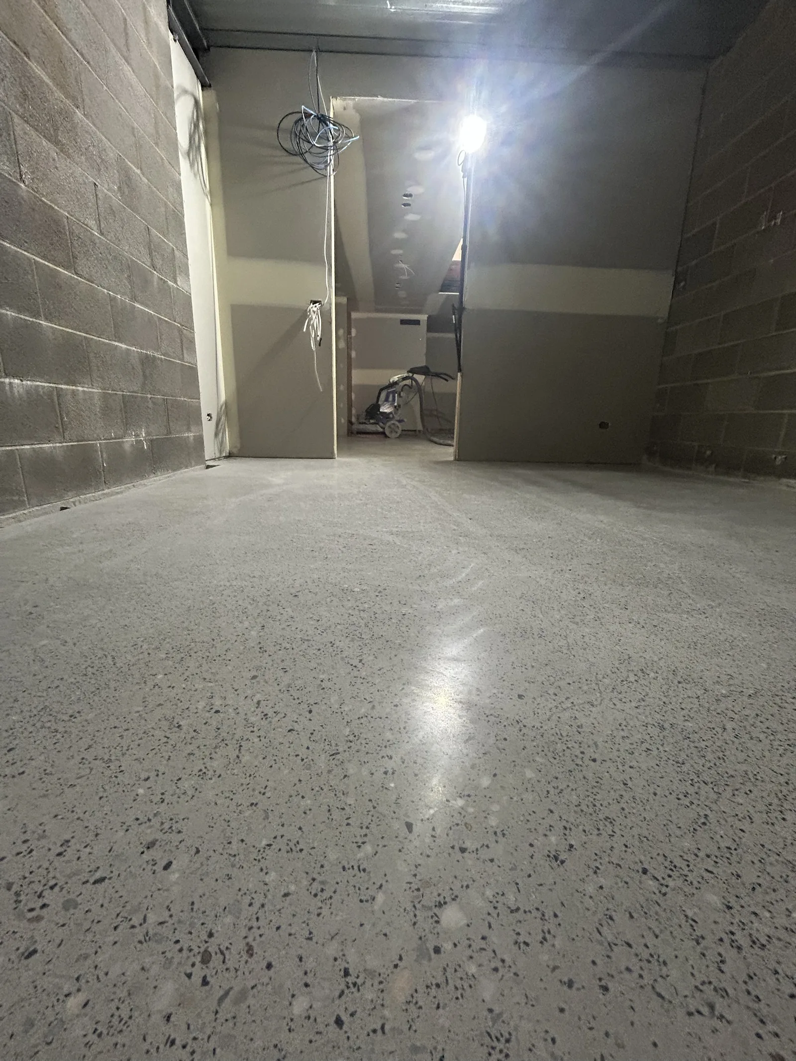 Freshly ground concrete floor with a glossy finish in a block-walled room, work light and grinder in the background