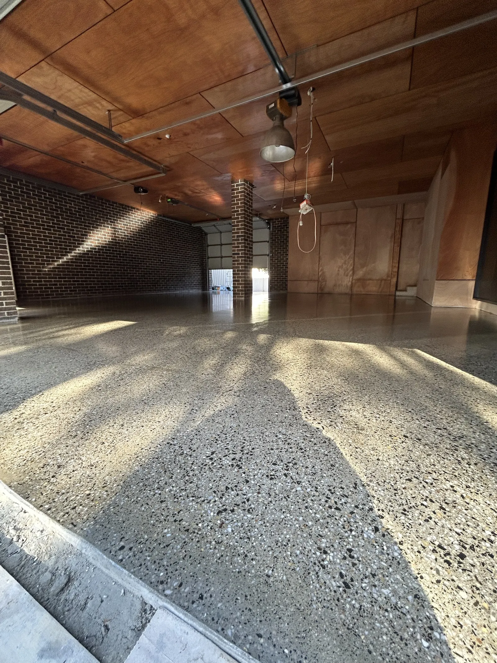 Grind and seal concrete in a brick-walled garage, low sun across the high-gloss exposed aggregate