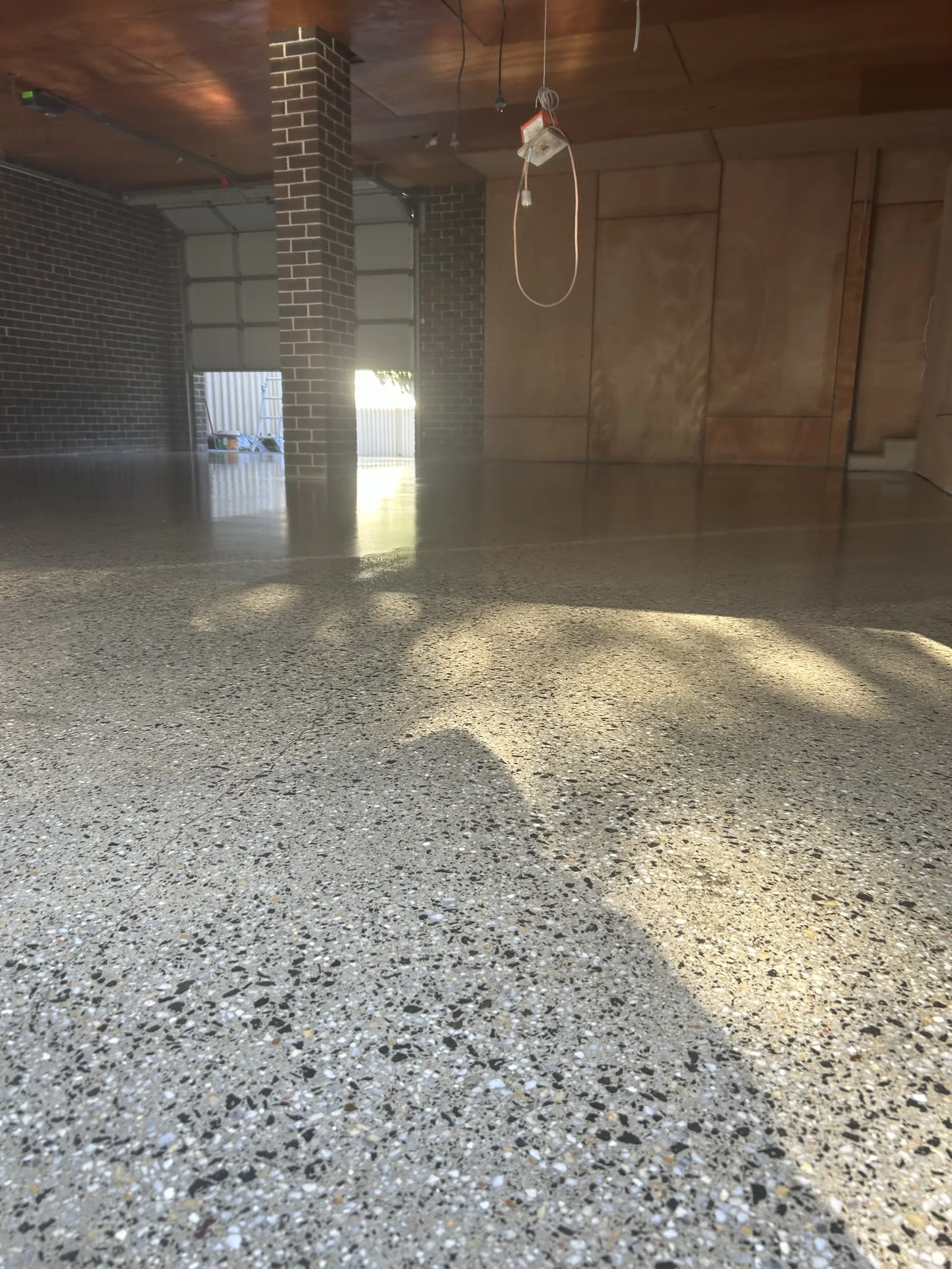 High-gloss grind and seal floor beside a brick pier, light from the roller door reflecting across it