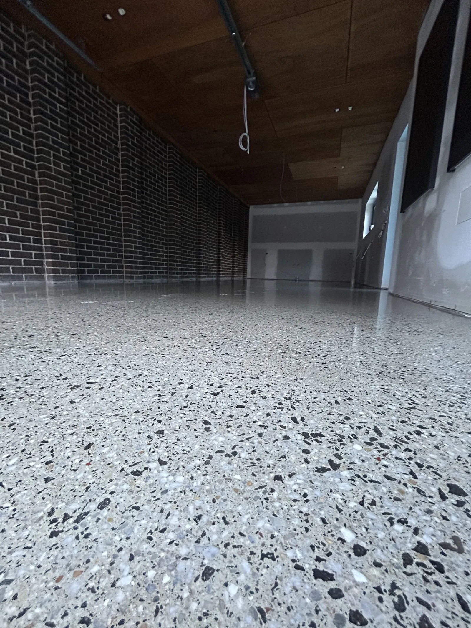 Low-angle close-up of a grind and seal floor with dark and white aggregate, brick wall and timber ceiling