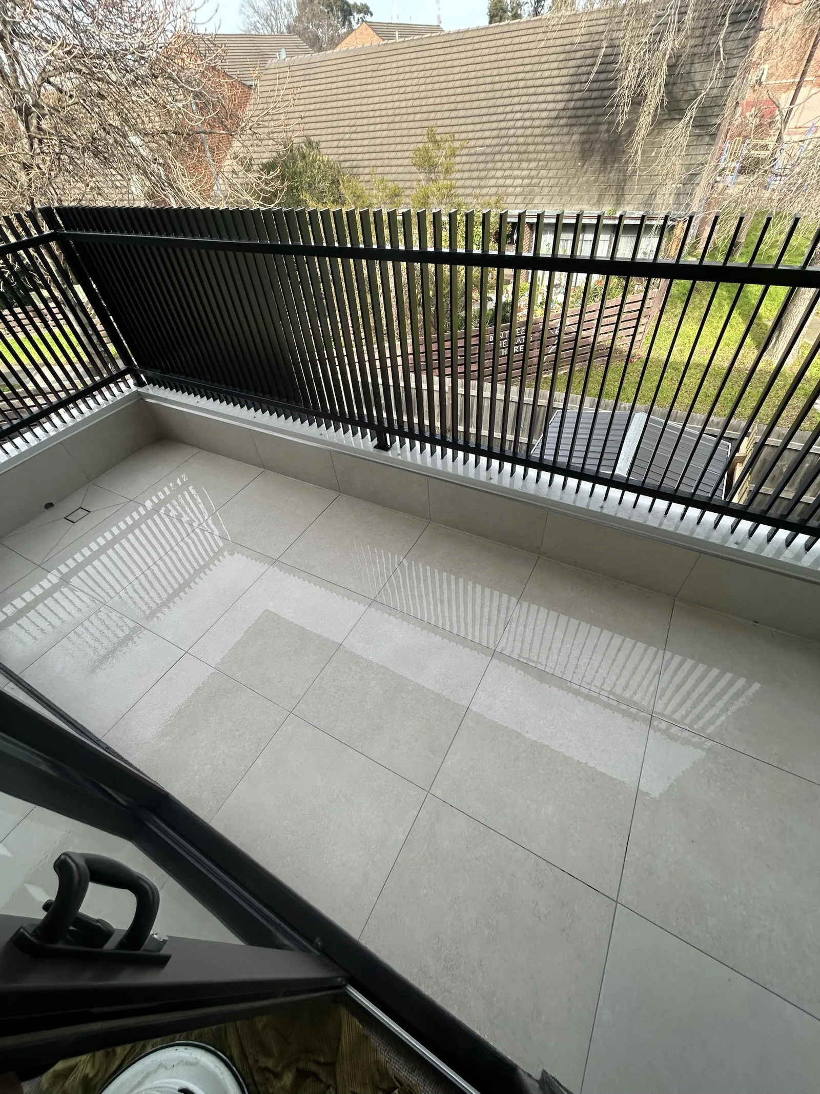 Large-format tiled balcony with a black batten balustrade, the slats reflecting in the tiles