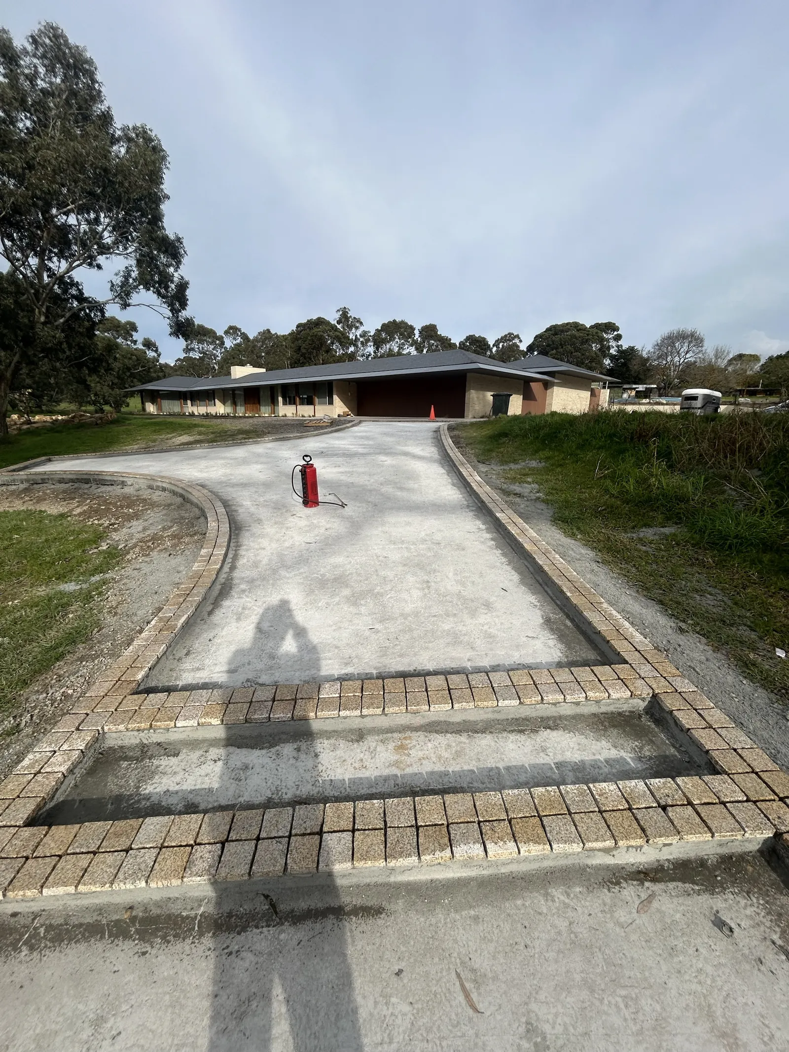 Concrete driveway edged with granite cobbles leading to a long single-storey home